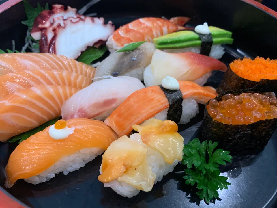 Sushi Haru의 연어 스시, 새우, 문어, 알, 초록 장식이 담긴 검은 접시
