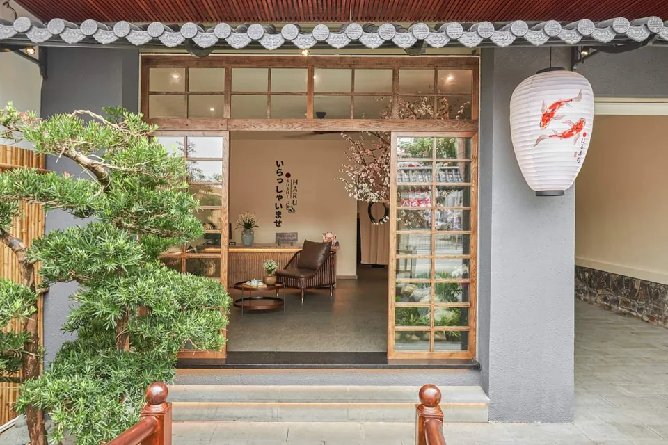 Mặt tiền Sushi Haru với cửa gỗ, đèn lồng cá koi và cây xanh trước lối vào
